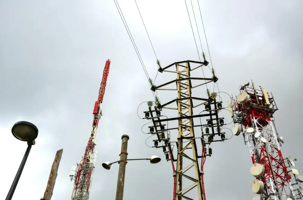 Close-up of tall transmission towers and telecom masts against a cloudy sky.